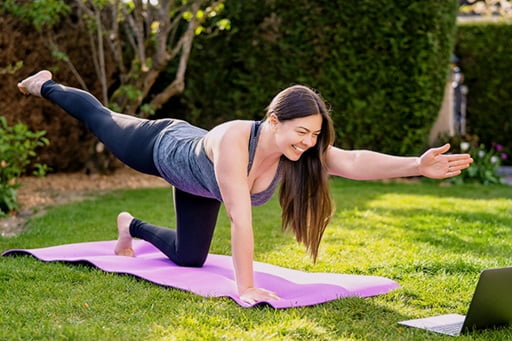 Frau macht Yoga in ihrem Garten vor dem Laptop